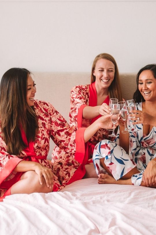 bridesmaid wearing red floral robes and drinking champagne