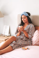 Recovering on bed wearing pastel leopard midi robe with tea and eye mask
