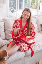 Red floral robe wearing ugg boots eating chocolates on the sofa